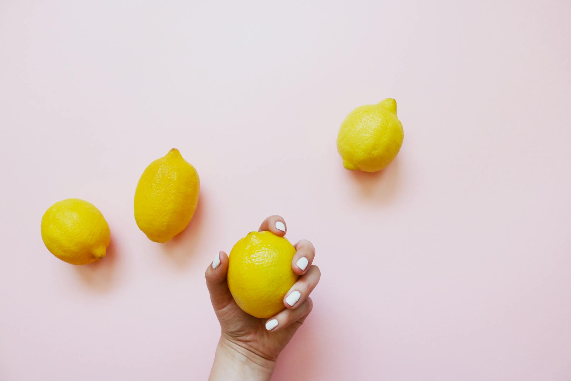 Hand holding a fresh lemon against a soft pink background, symbolizing the sensation and gentleness of clitoral suction technology