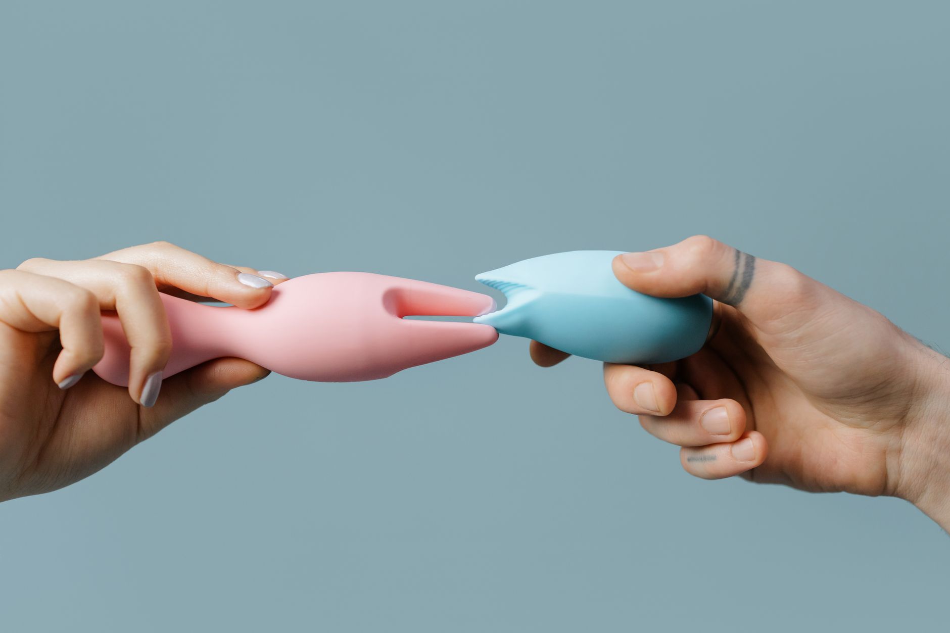 Hands holding pastel-colored lemon vibrators and adult toys on a neutral background