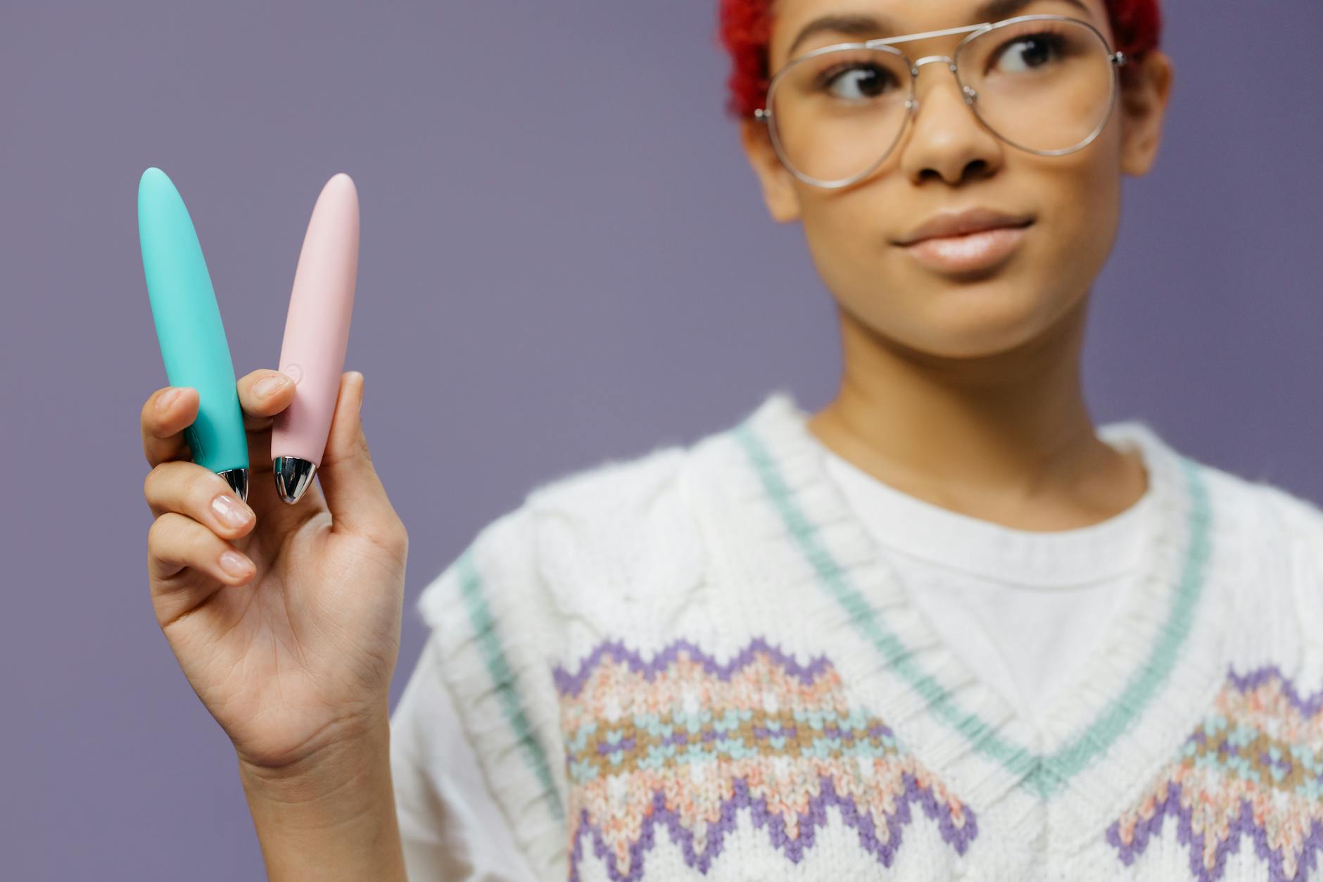 A woman holding colorful vibrators against a purple background, representing self-pleasure and sexual wellness