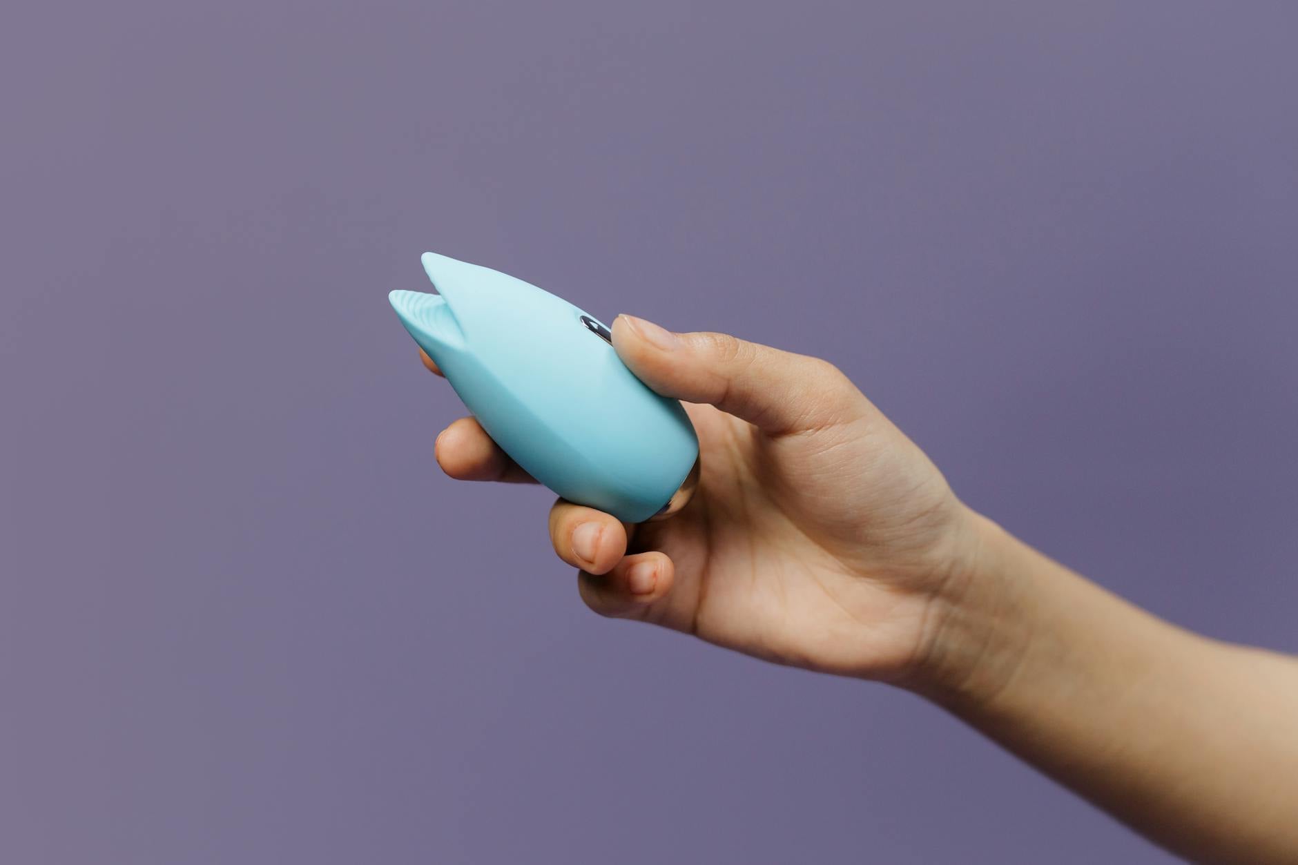 A blue silicone lemon clitoral vibrator held in hand against a solid purple background