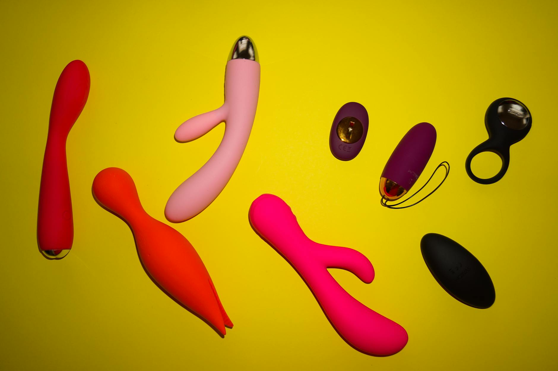 Array of colorful sex toys including vibrators arranged on a bright yellow surface