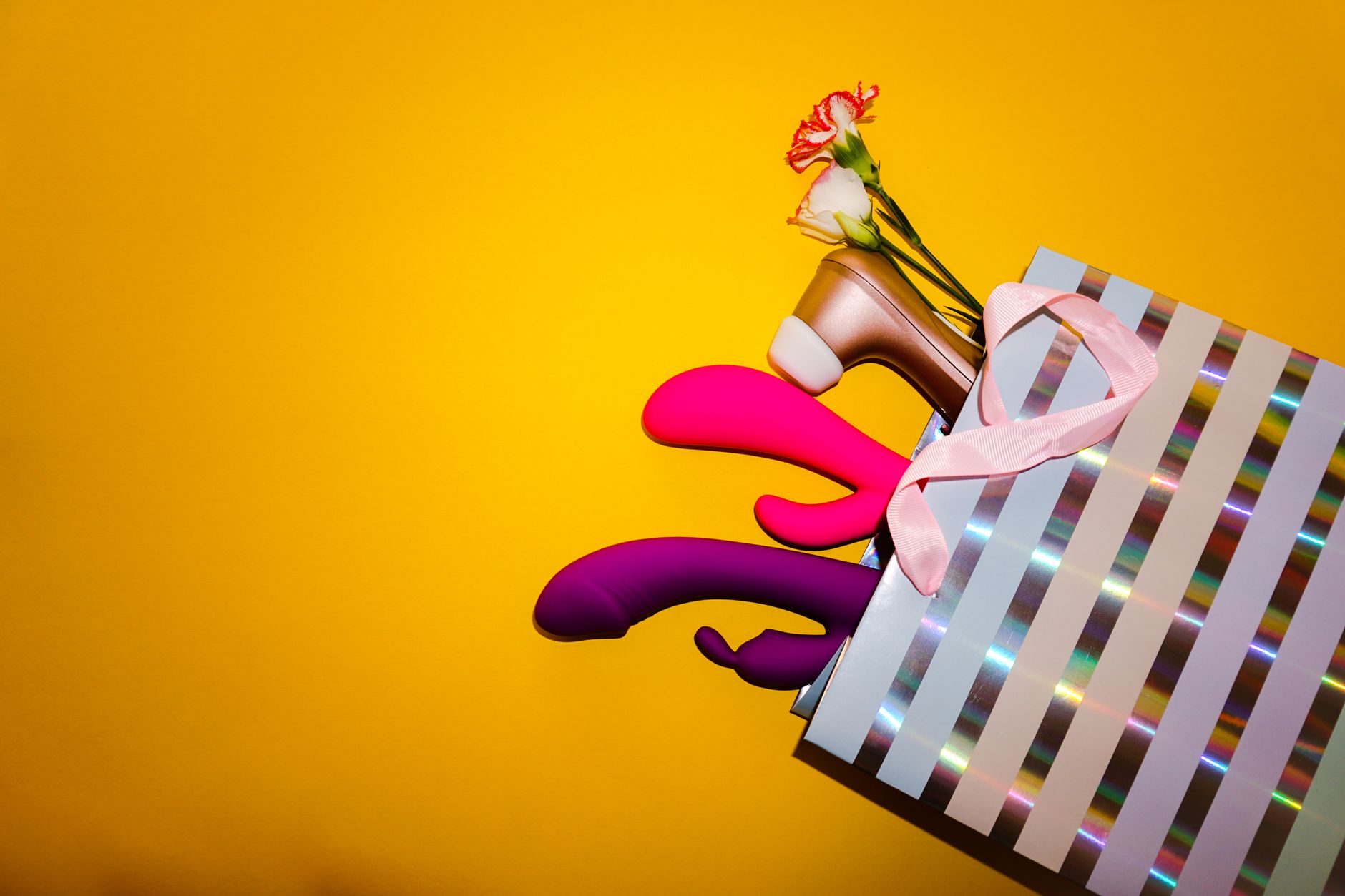 Close-up of a hand holding an orange vibrator against a minimalistic purple backdrop