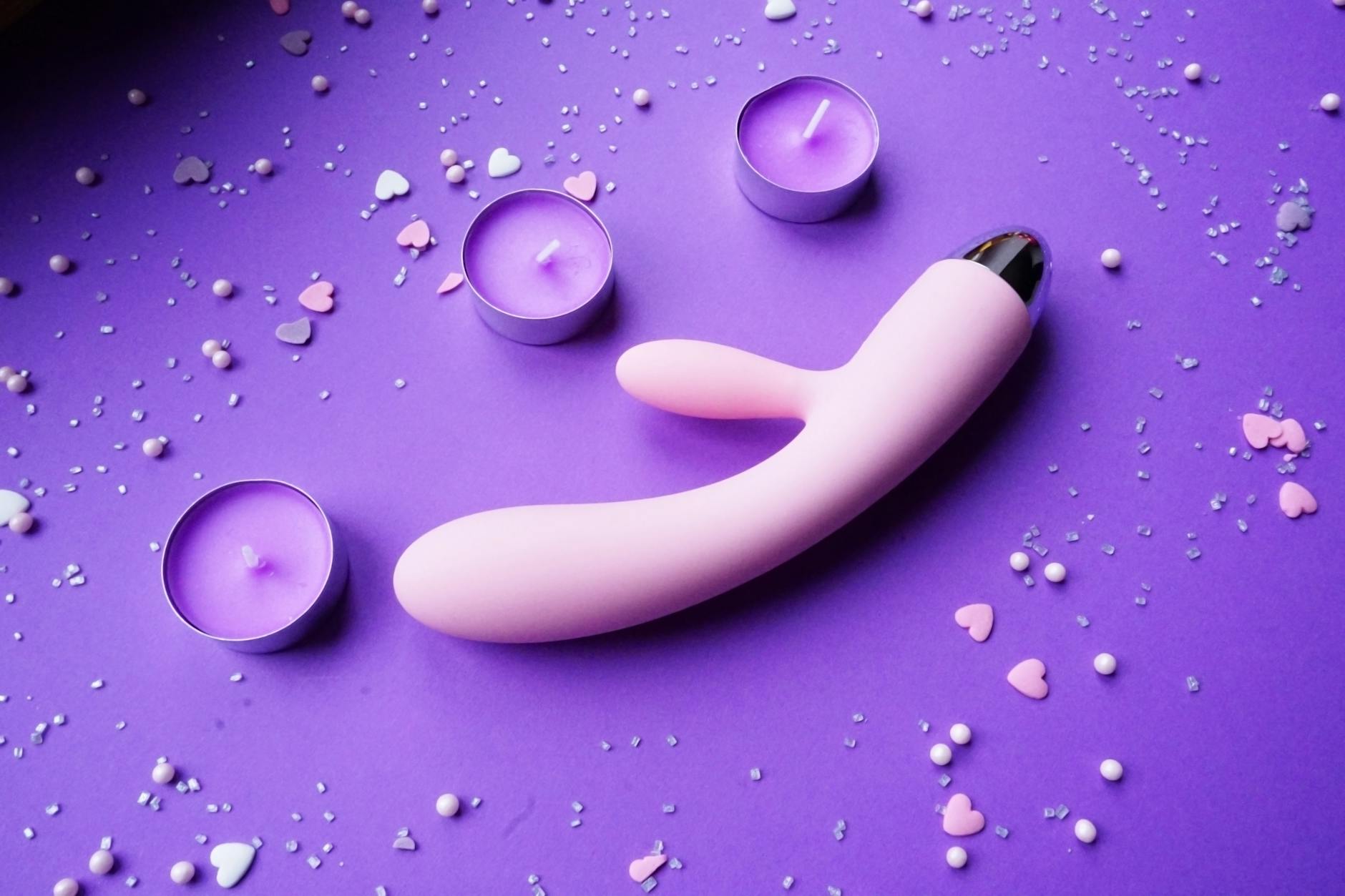 Pink vibrator on a purple background with heart confetti and candles, symbolizing self-love and personal pleasure after divorce.
